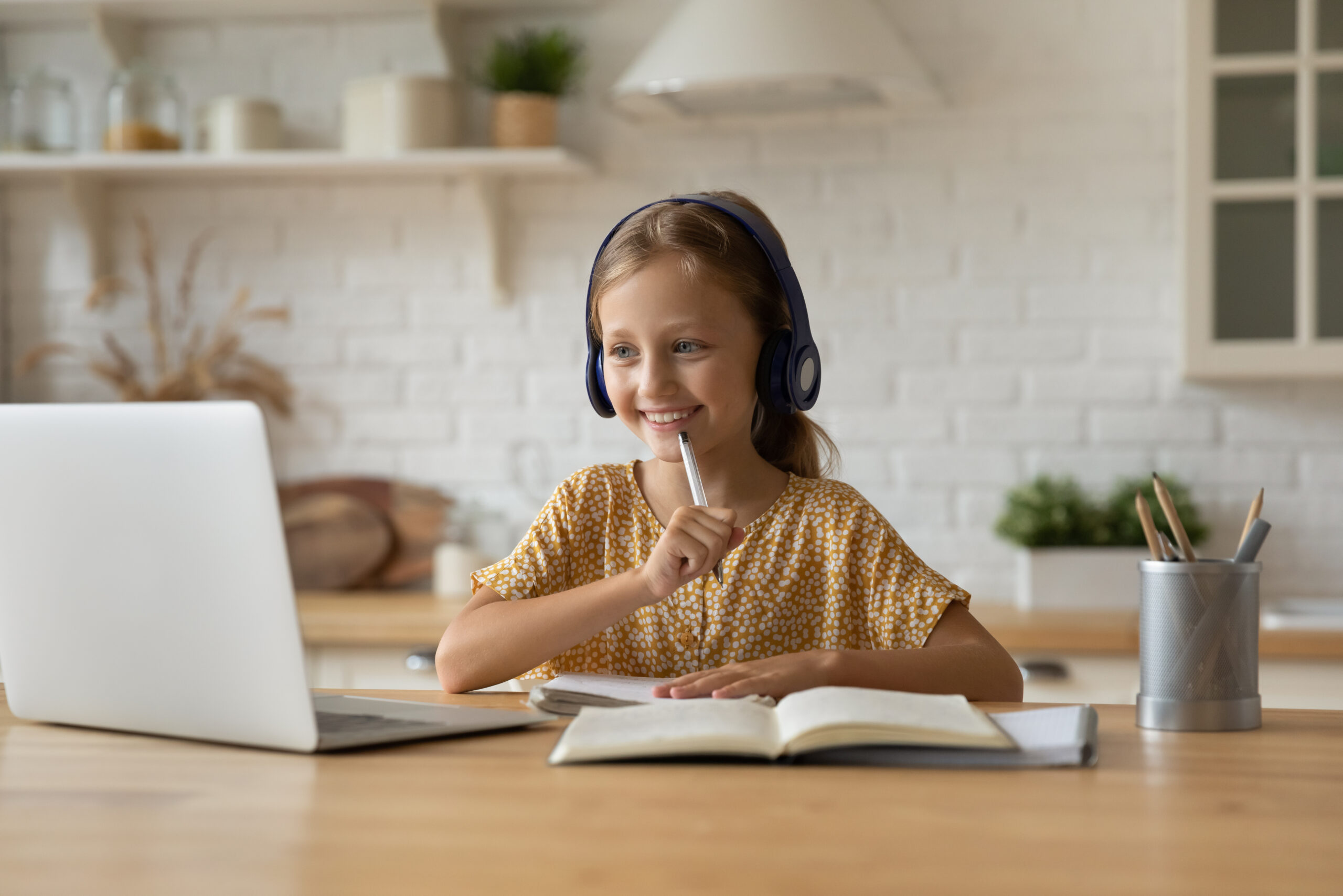 Smiling little Caucasian girl in headphones looking at laptop screen