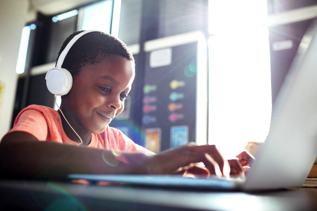Close up of boy listening music while using laptop at desk in school